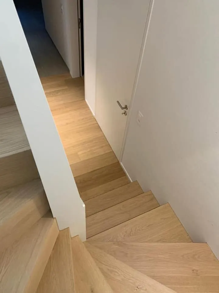 Treppe mit Eichenstufen zwischen weissen Wänden, von oben fotografiert